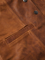 Close-up of whiskey-brown leather vest chest pocket, buttons, and stitching