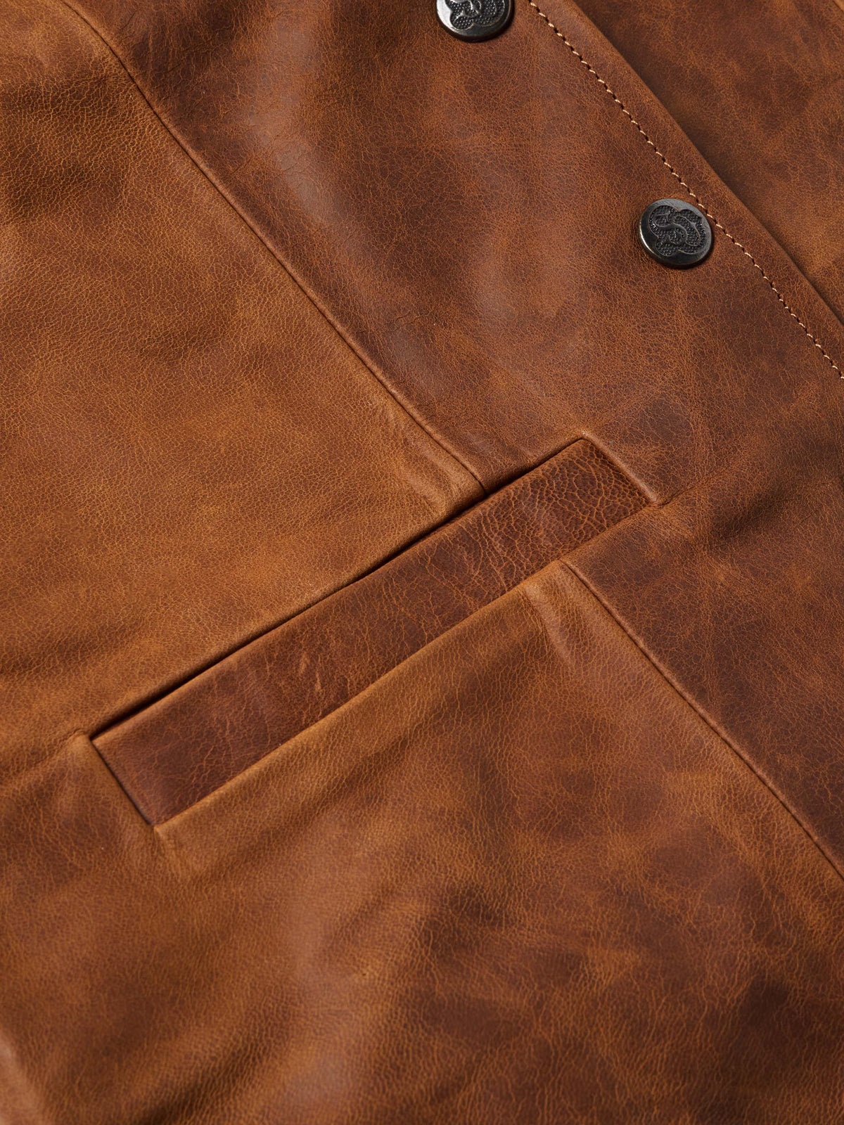 Close-up of whiskey-brown leather vest chest pocket, buttons, and stitching